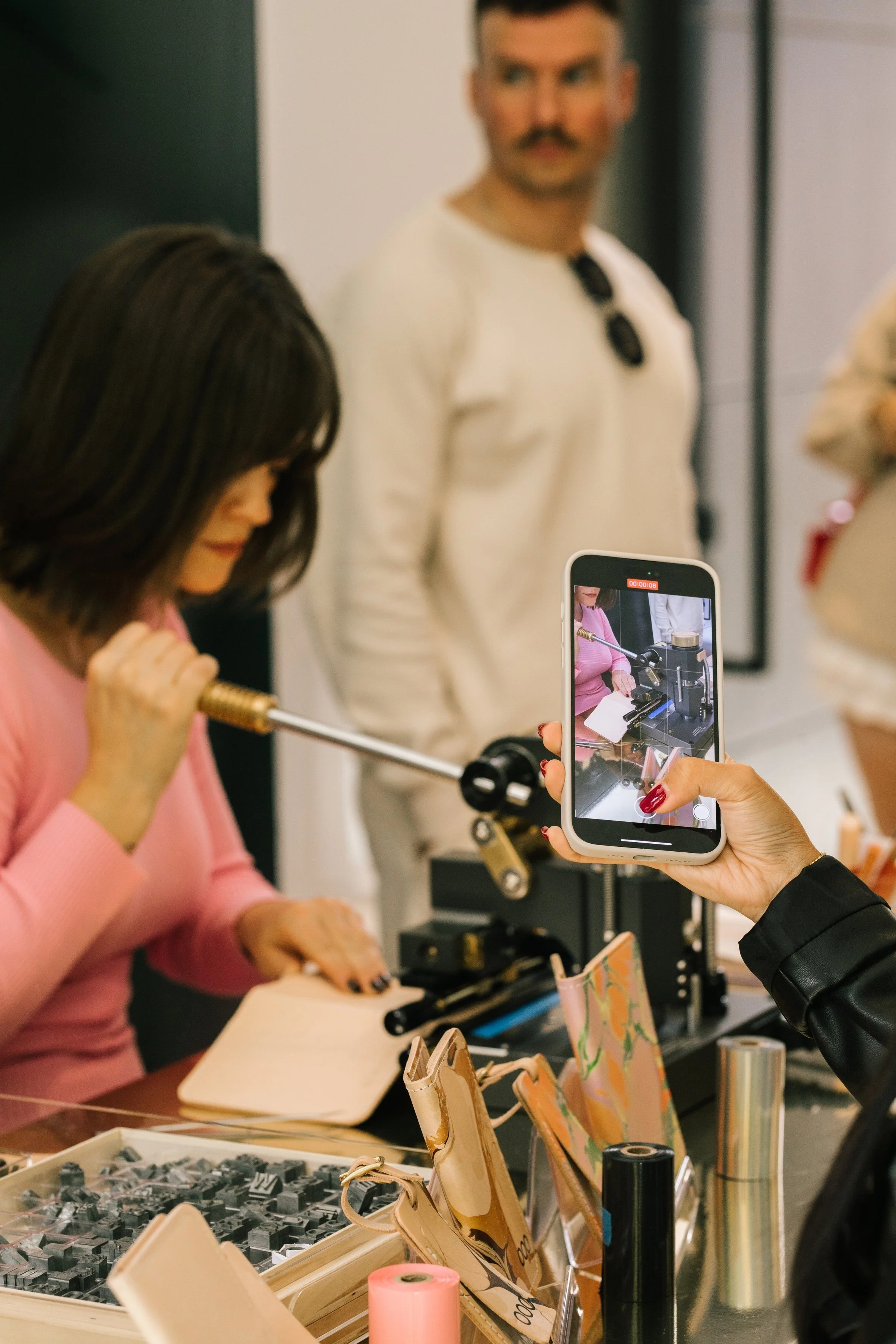 Woman at a leather embossing station with smartphone recording