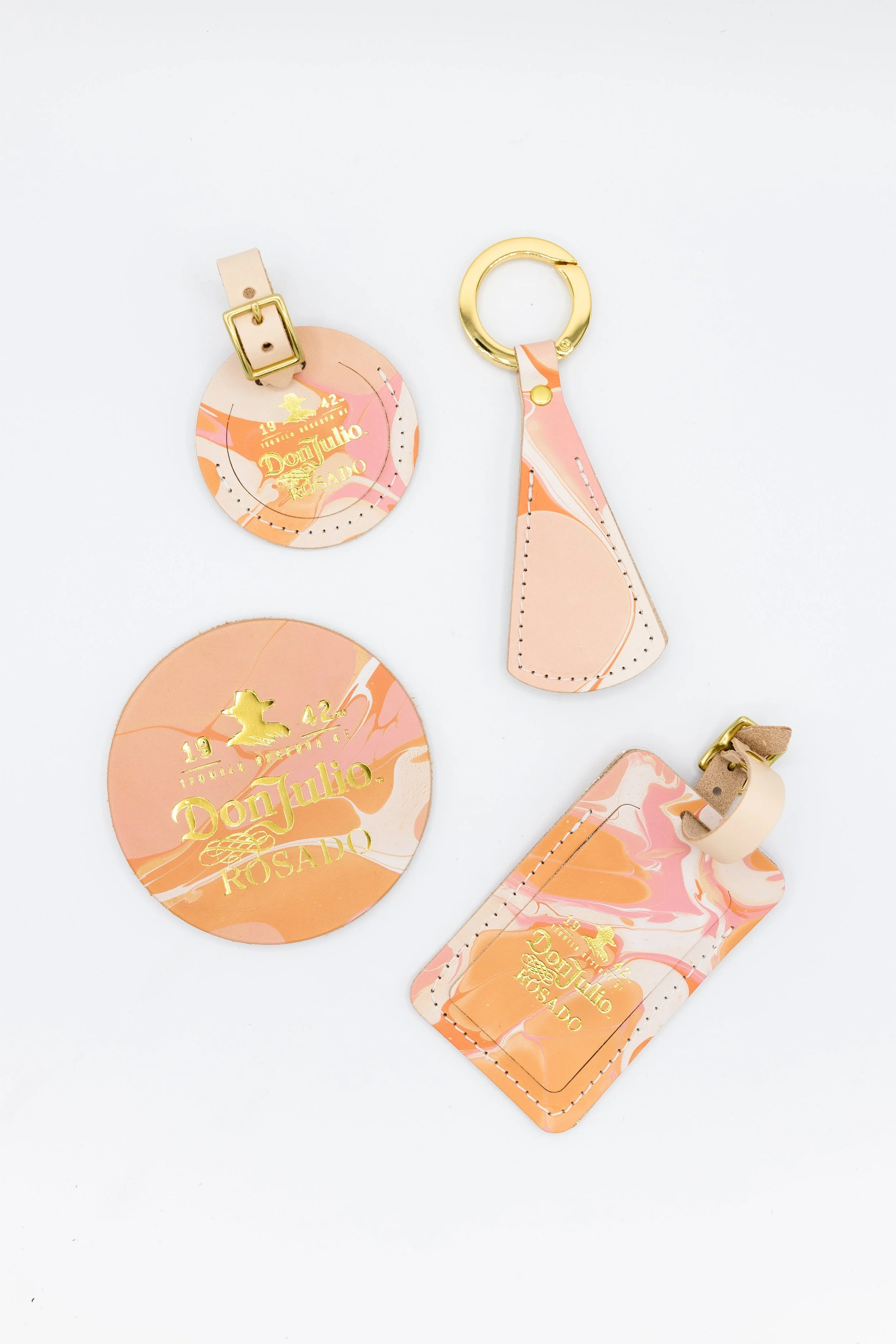Don Julio Rosado branded leather accessories including round and rectangular tags with gold text, and a leather hat clip with gold ring, featuring pink and orange marbled design.