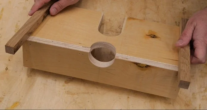hands holding a wooden piece each to the bottom of a homemade router table fence on top of a wooden workbench
