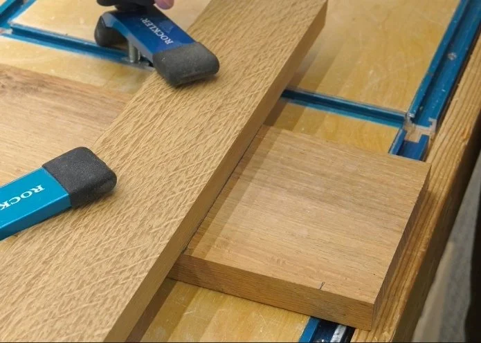 using a straight piece of wood along the marked line of another piece of wood, held down by clamps