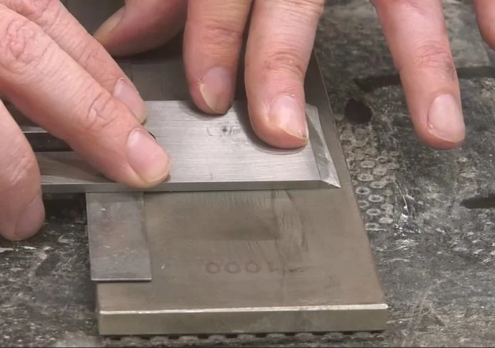 a plane iron raised slightly by a metal ruler on the opposite edge, ontop of a diamond stone