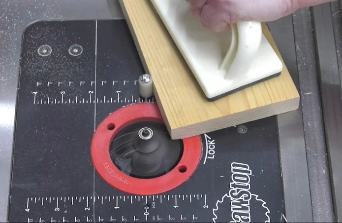 a router table starter pin creating a fulcrum for the wooden workpiece as it is guided towards the router bit