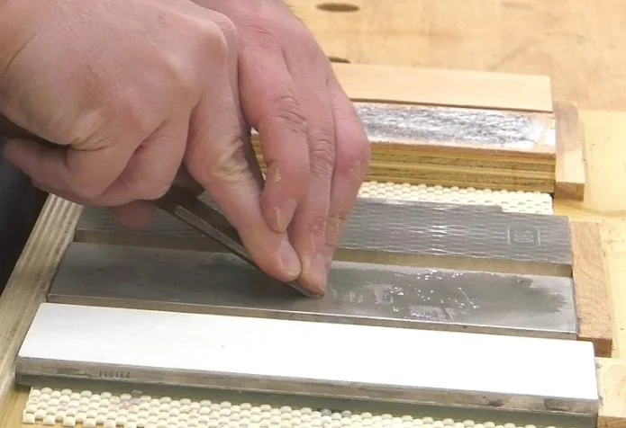 hands holding the bevel of a chisel down on a diamond stone for sharpening