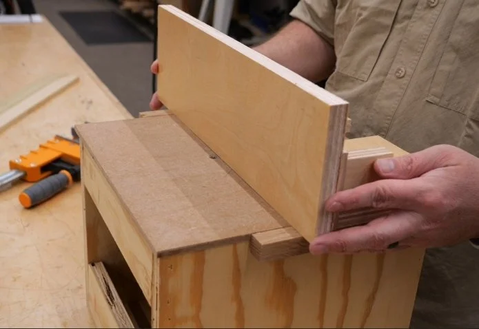 hands holding a piece of plywood up to a diy router fence