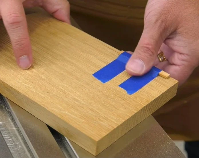 taping a shim to a work piece using blue tape on the edge of a metal router table top