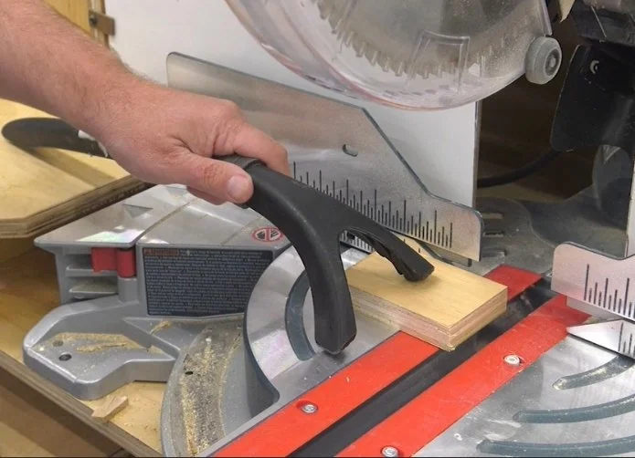 a plastic holding stick with forked end holding down a small work piece on a miter saw to keep hands safe.