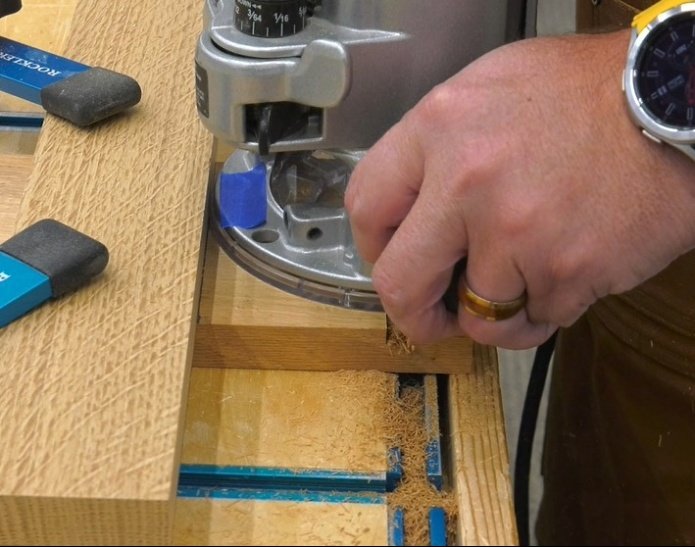hands holding a router and making a cut on a piece of wood