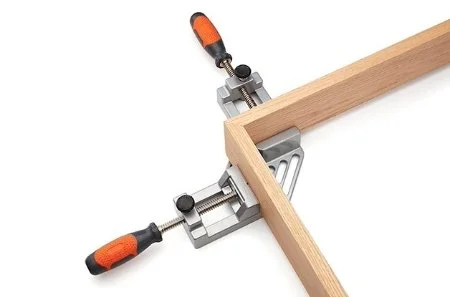 metal miter clamp with orange and black handles holding a wooden miter in place