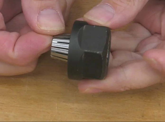 hands holding a self releasing collet from a router on a wooden workbench table top