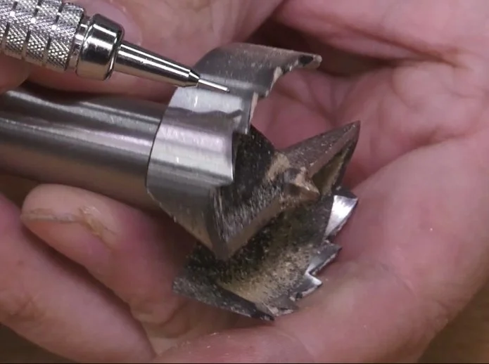 a mechanical pencil tip pointing at a saw-toothed forstner bit rim