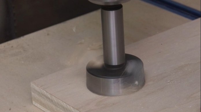 a forstner bit cutting a hole in a piece of plywood