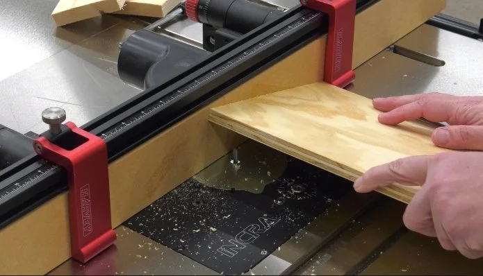 lowering a piece of plywood down onto a spinning bit in a router table, while the piece of plywood is being braced by a flip stop on the router fence