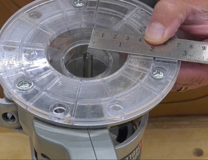 a hand using a ruler to measure from the center of a router bit installed in the router, to the outside edge of the router plate