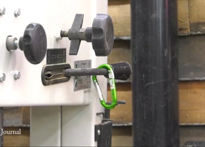 bright green carabiner clipped to the tension-release lever of a band saw