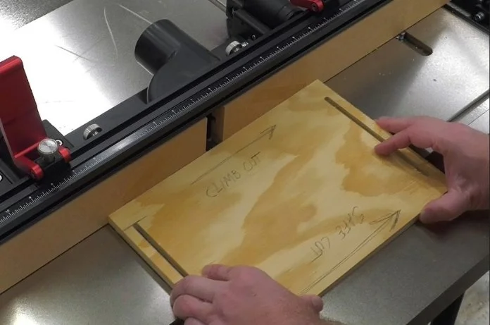 a piece of plywood with writing on it, on top of a router table, indicating which direction is a dangerous climb cut
