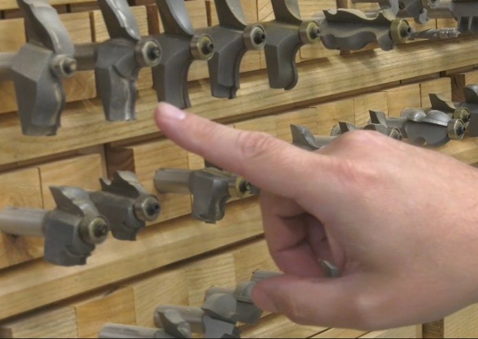 a hand pointing at large router bits used for creating profiles for table top, in front of other router bits