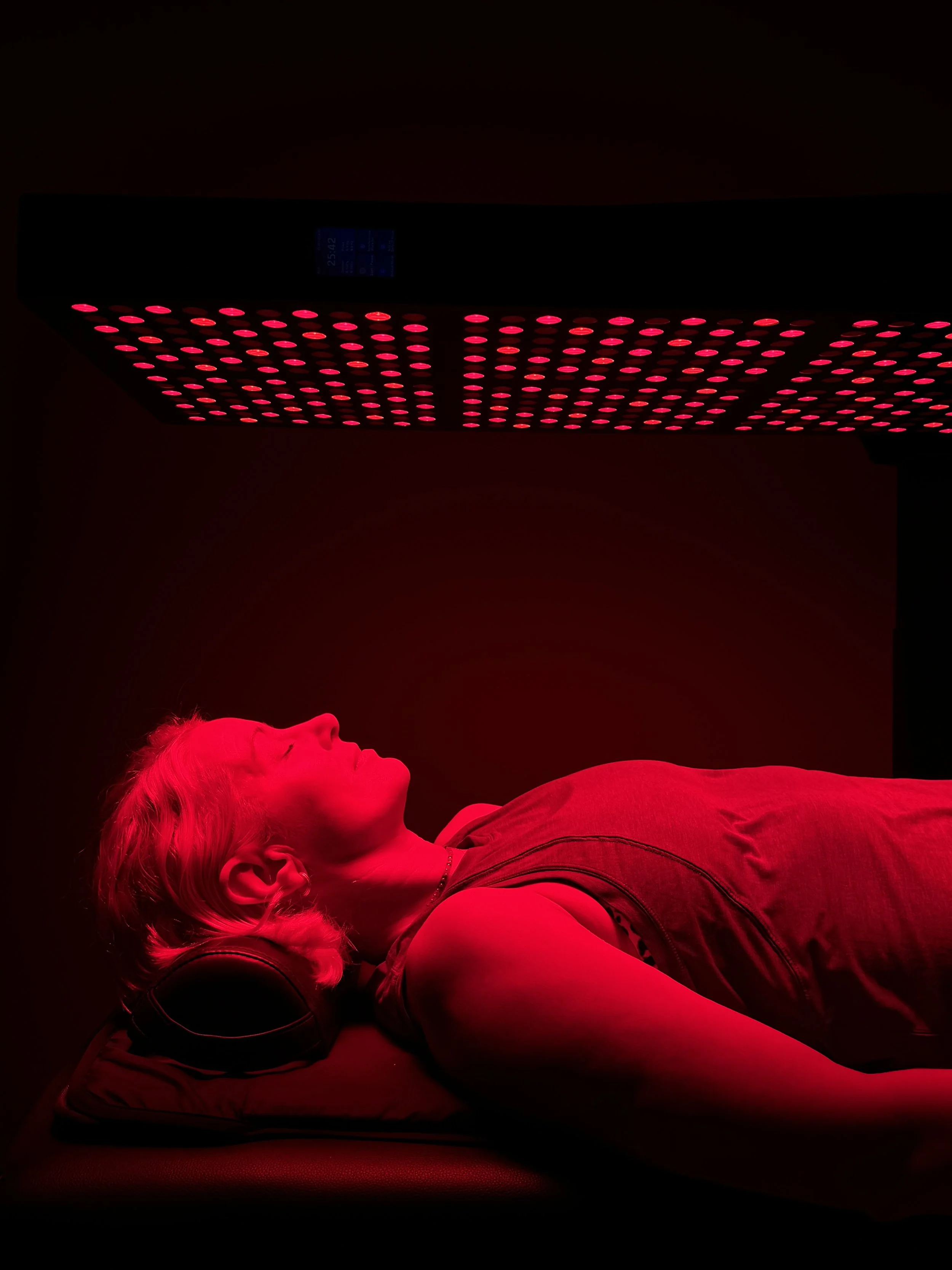 Client receiving full-body red light therapy under LED panel for recovery and nervous system support