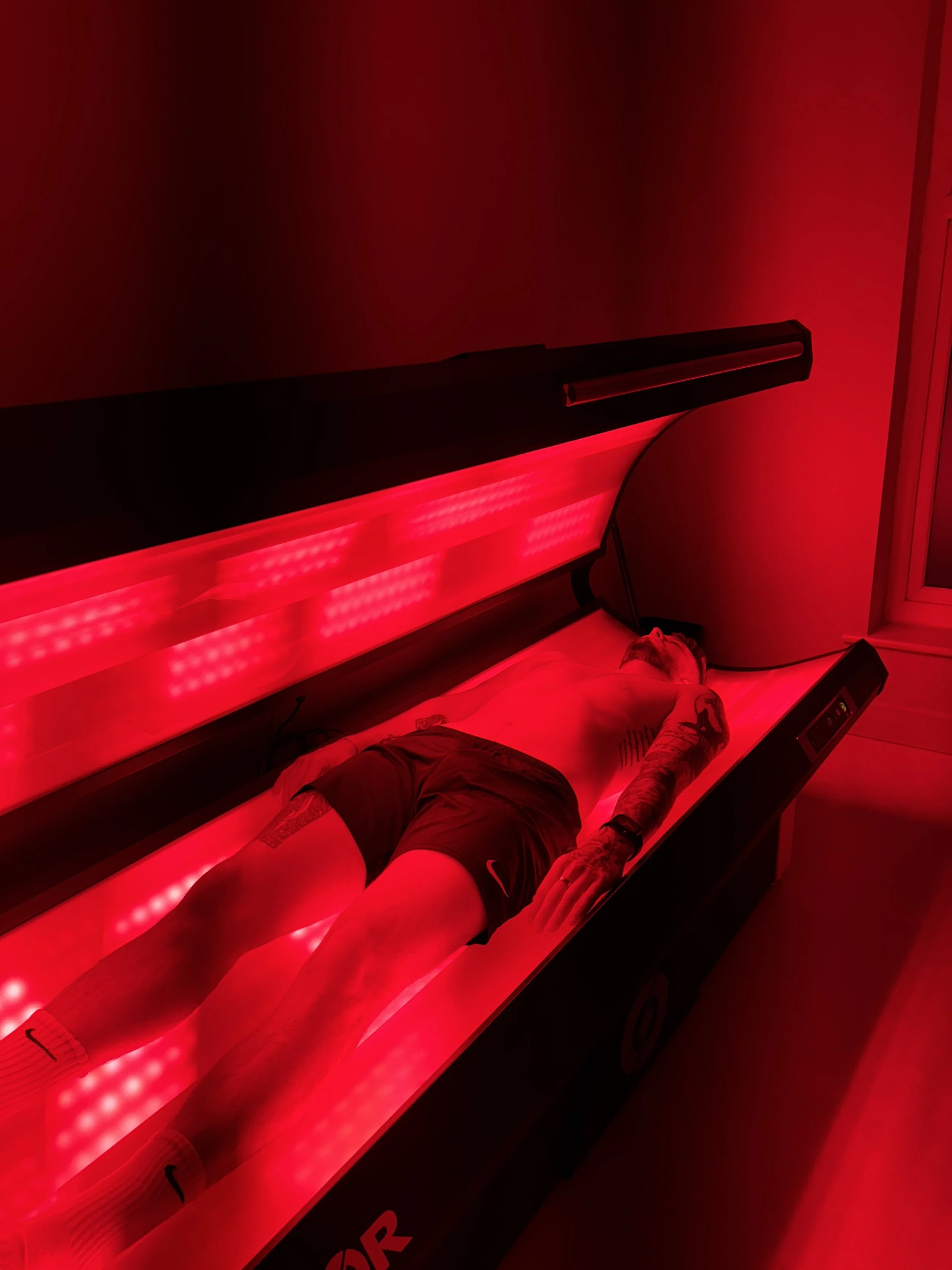 Client lying inside NovoTHOR red light therapy bed during full-body photobiomodulation session at ReGen Rooms.