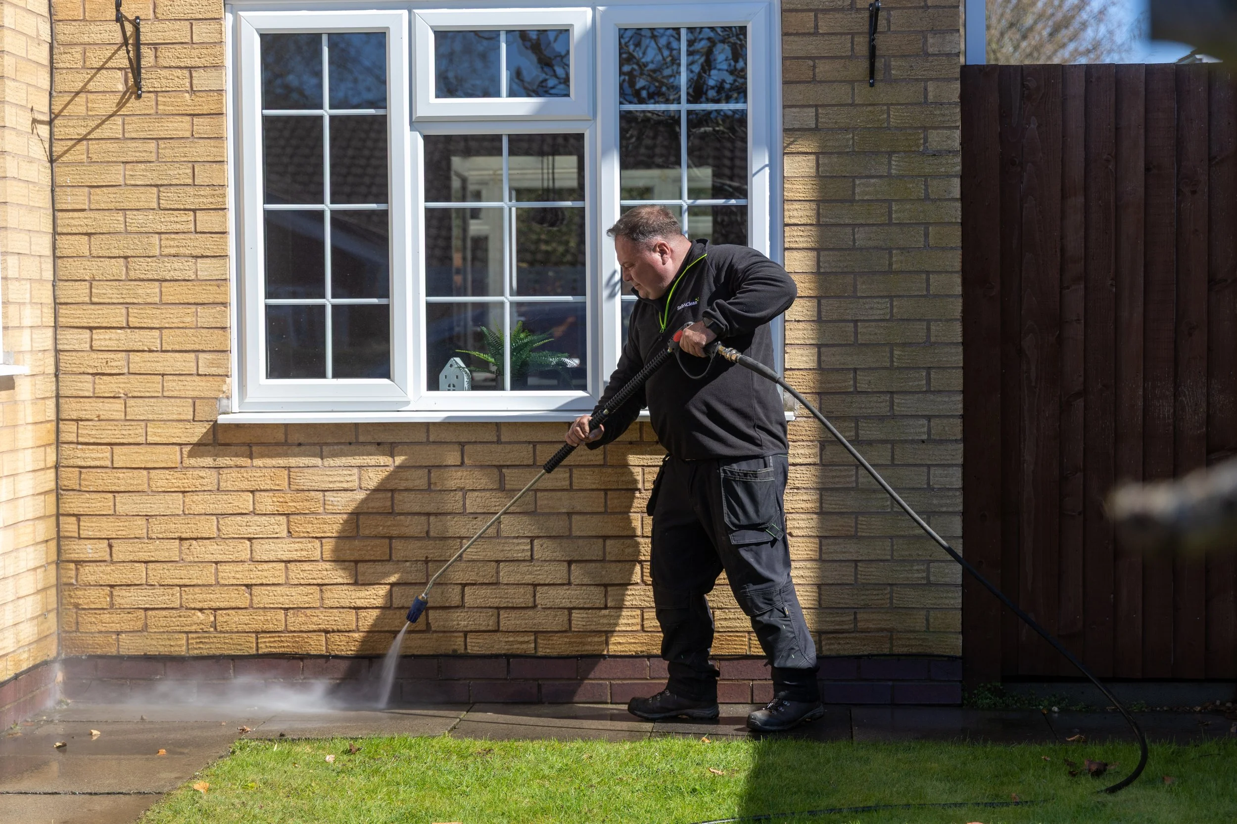 A man washing the concrete patio outside a house with a power washer.