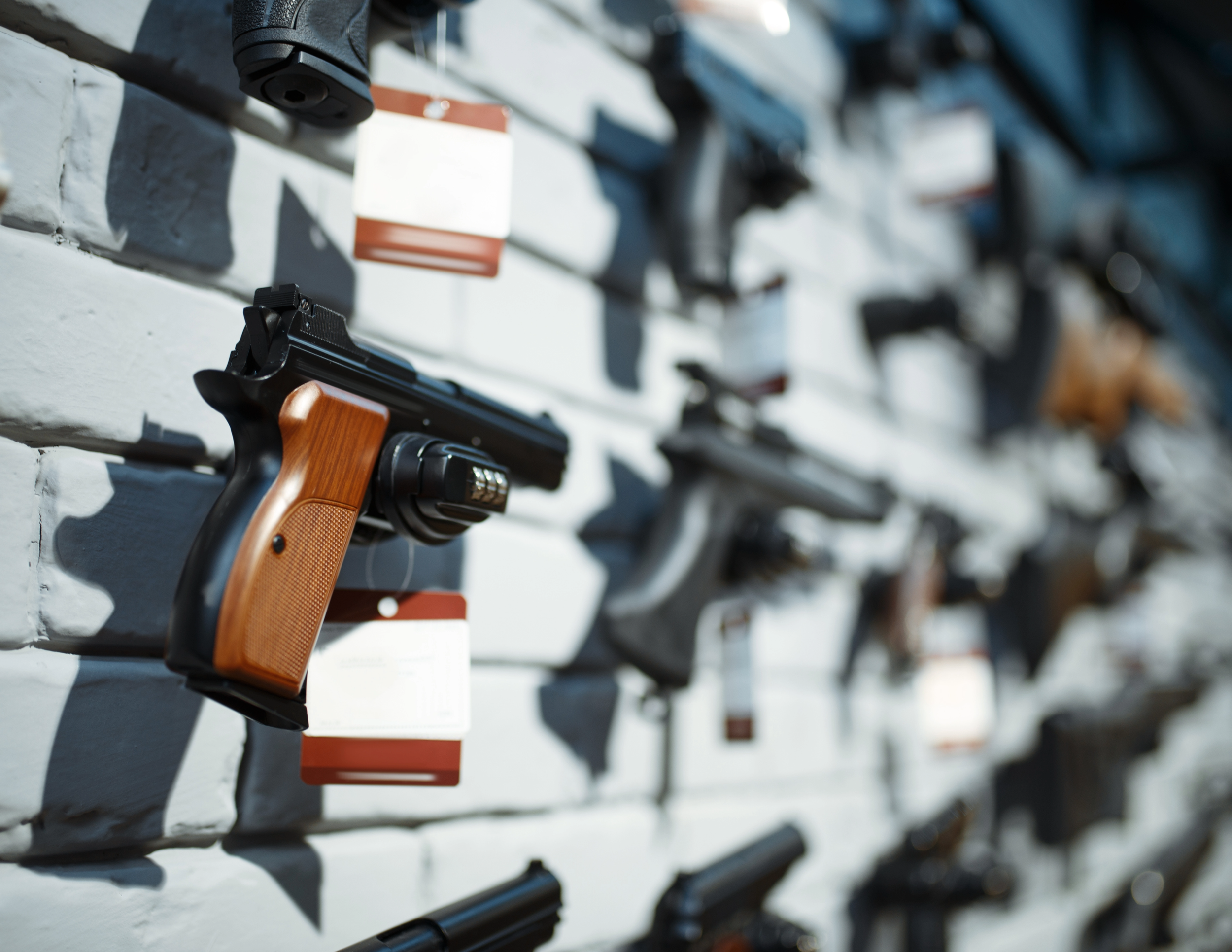A display of various handguns mounted on a white brick wall, with price tags attached.