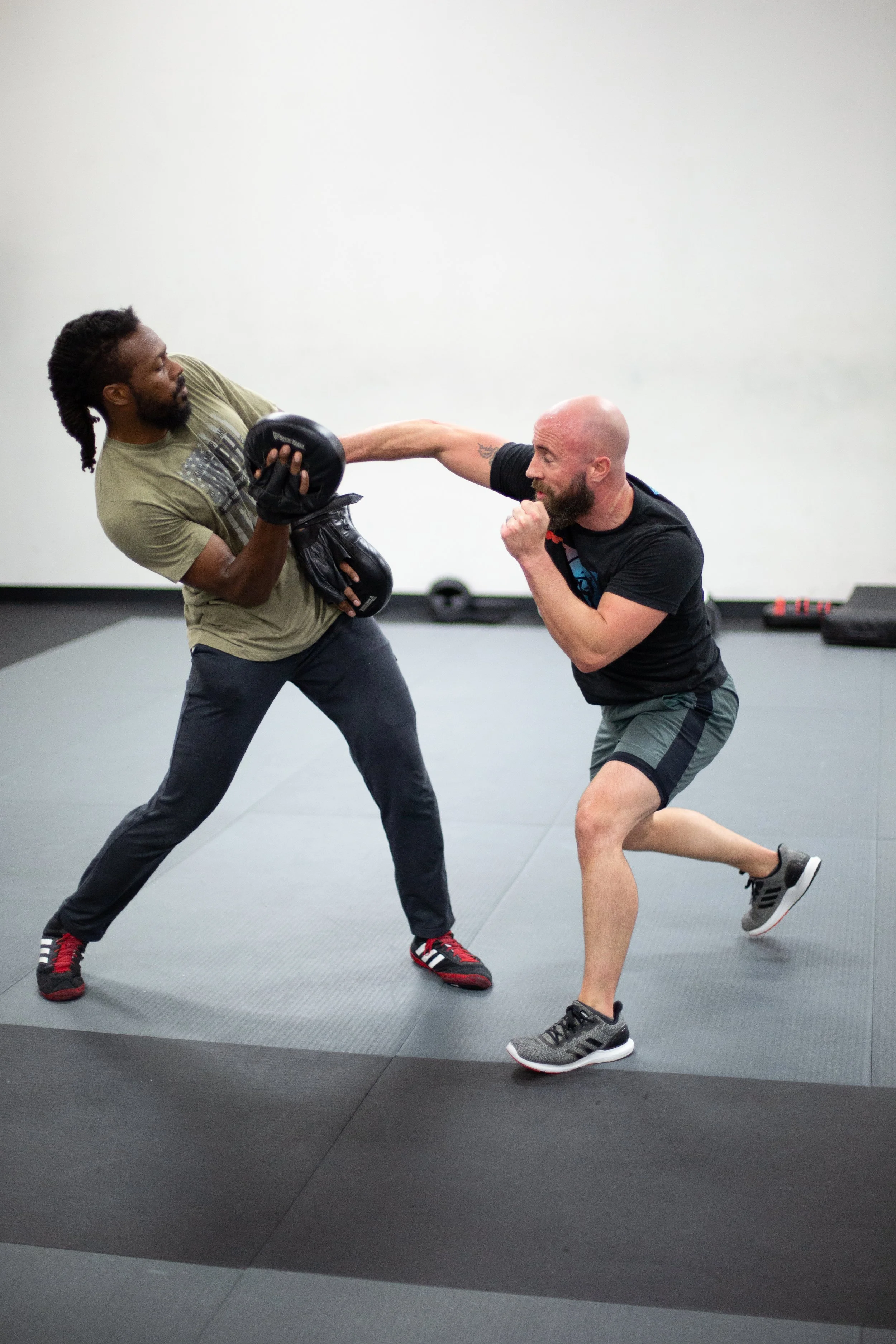 Two men practicing boxing, one punching while the other holds pads in a gym setting.