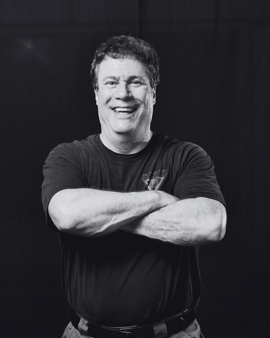 Black and white photo of a smiling man (Darren Levine) with arms crossed, wearing a T-shirt.