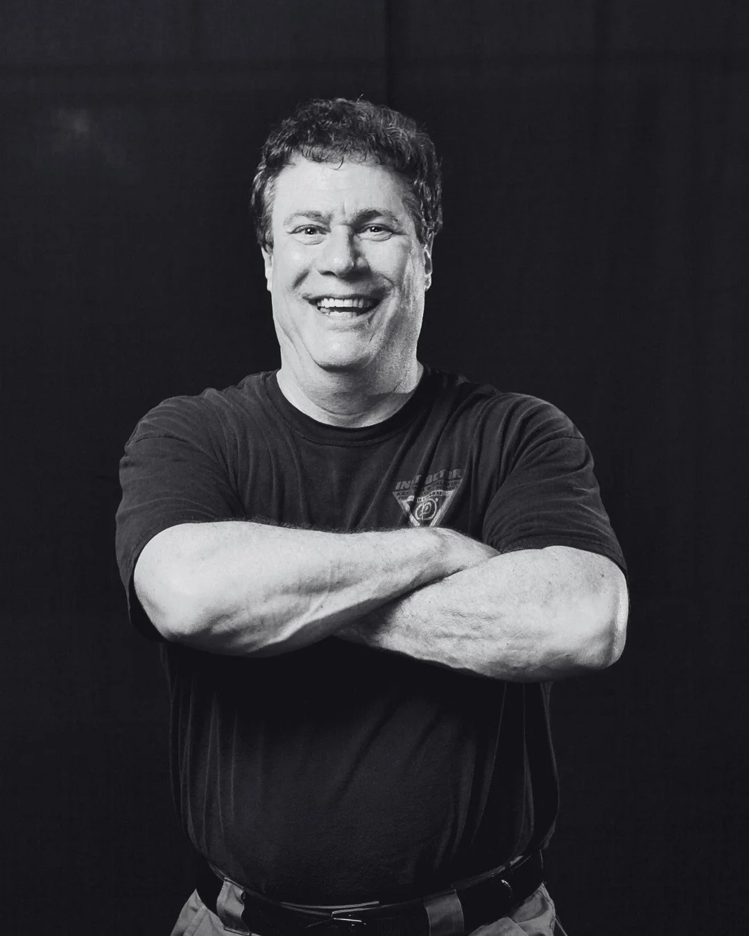 Black and white photo of a smiling man (Darren Levine) with arms crossed, wearing a T-shirt.