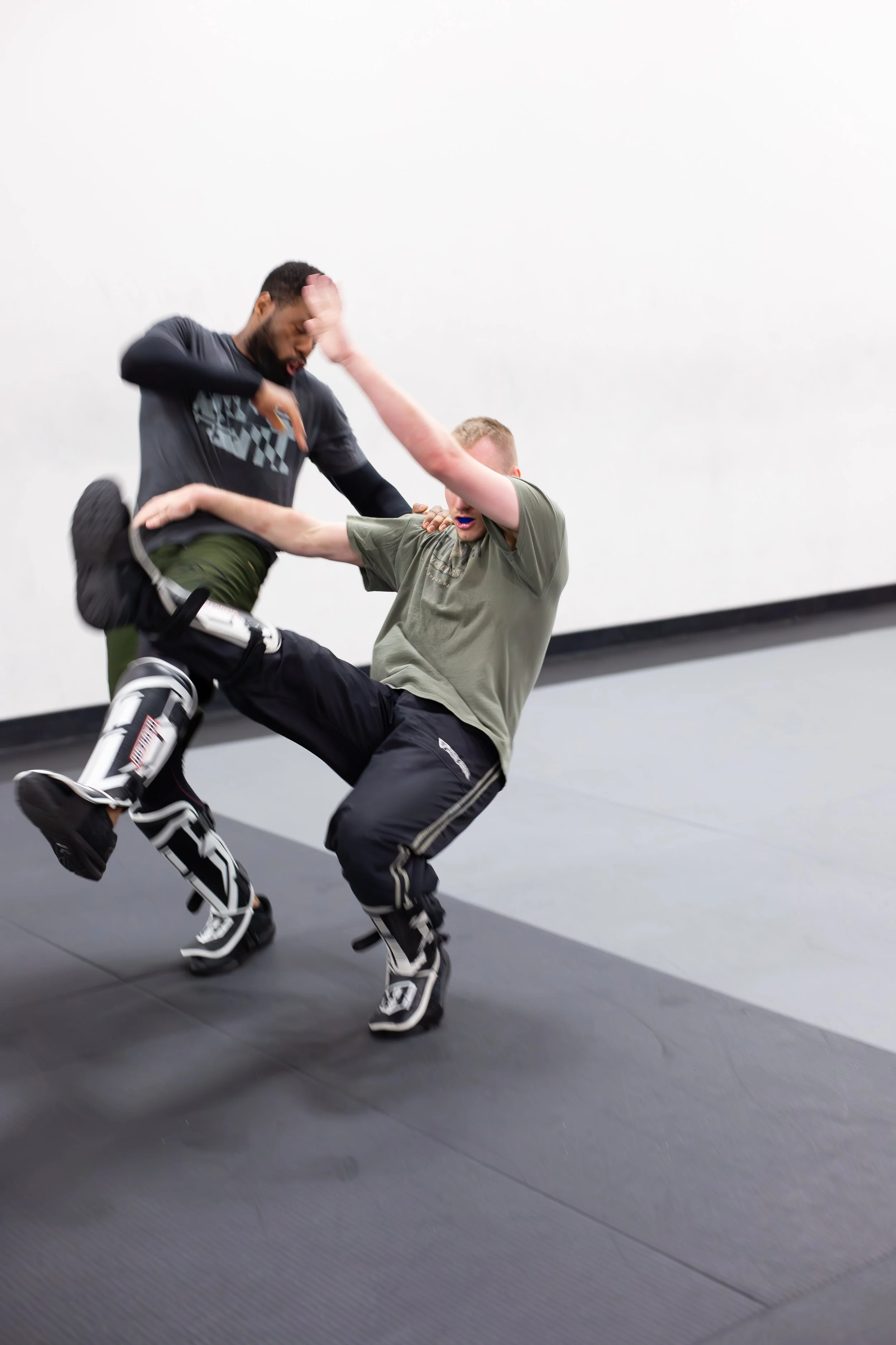 Two individuals practicing martial arts with protective gear on a mat.