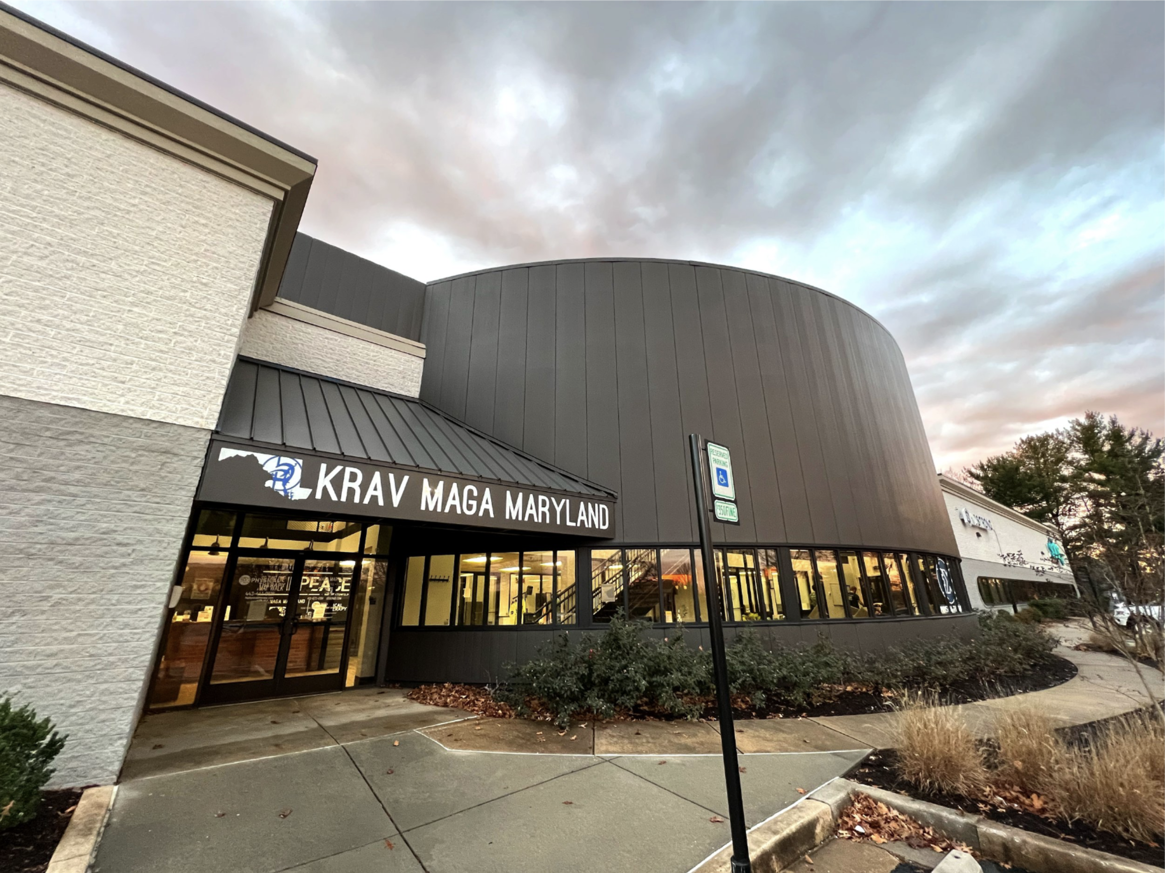 Exterior of Krav Maga Maryland self-defense studio with large windows and entrance visible under a cloudy sky.