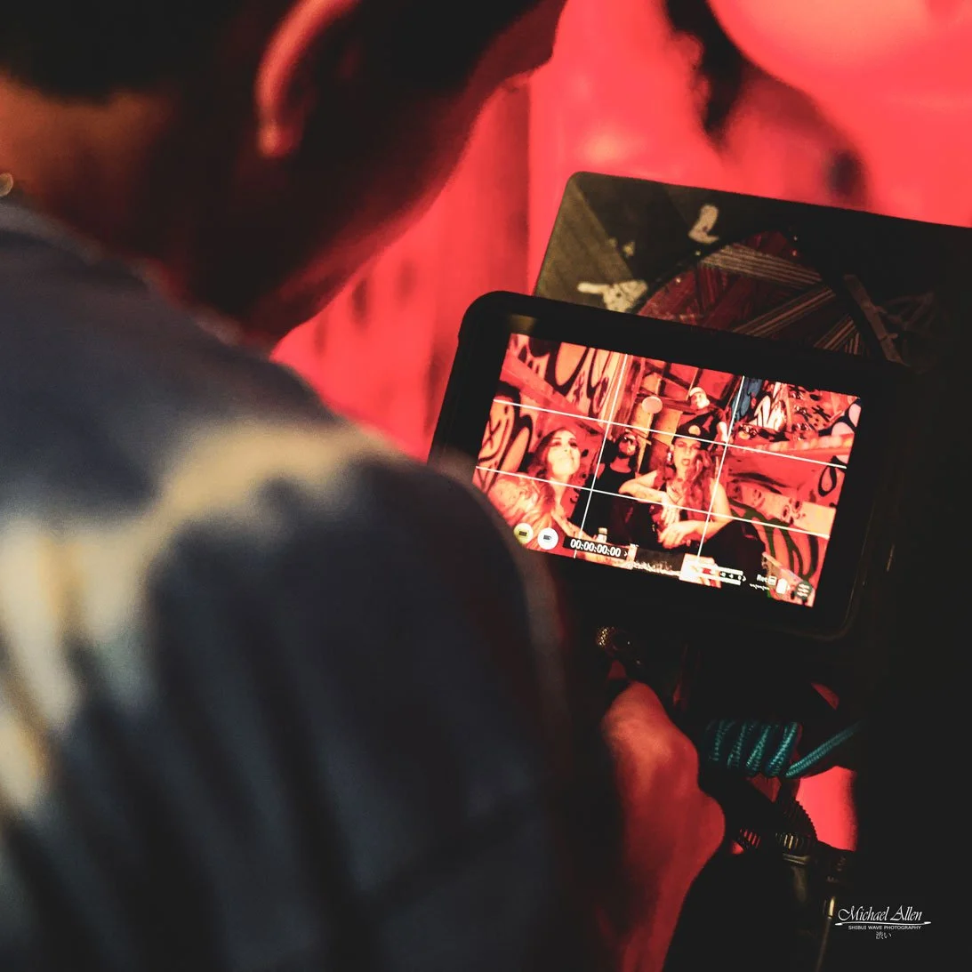 A person is recording or taking a photograph of three women sitting in front of a graffiti-covered wall, with a camera or smartphone.