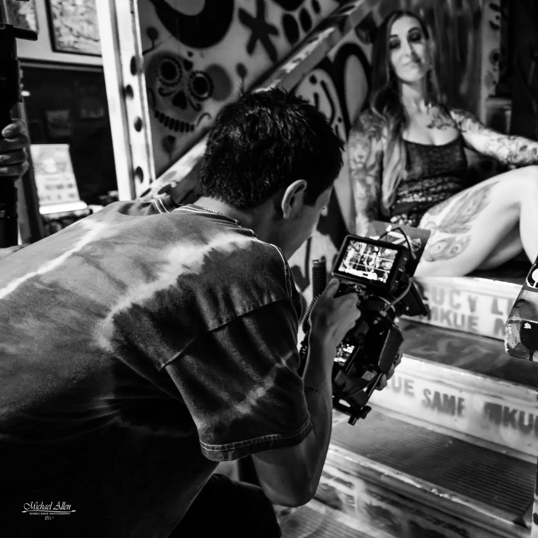 Photographer takes a black-and-white photo of a woman with tattoos sitting on a platform with graffiti background.