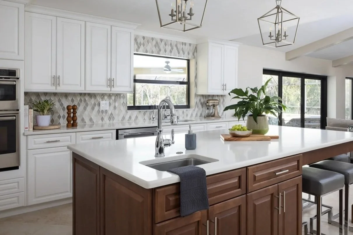 White kitchen with large center island, quartz countertops, patterned backsplash, and accessories including potted plant, bowl of fruit, books and stand mixer in Palm Harbor, FL.