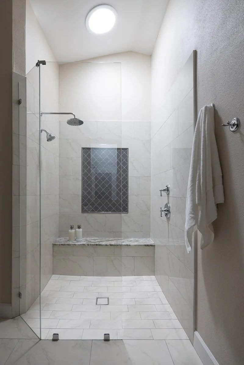 Large walk-in shower with marble-look porcelain tile and marble built-in bench. Glass shower surround and skylight in Clearwater, FL.