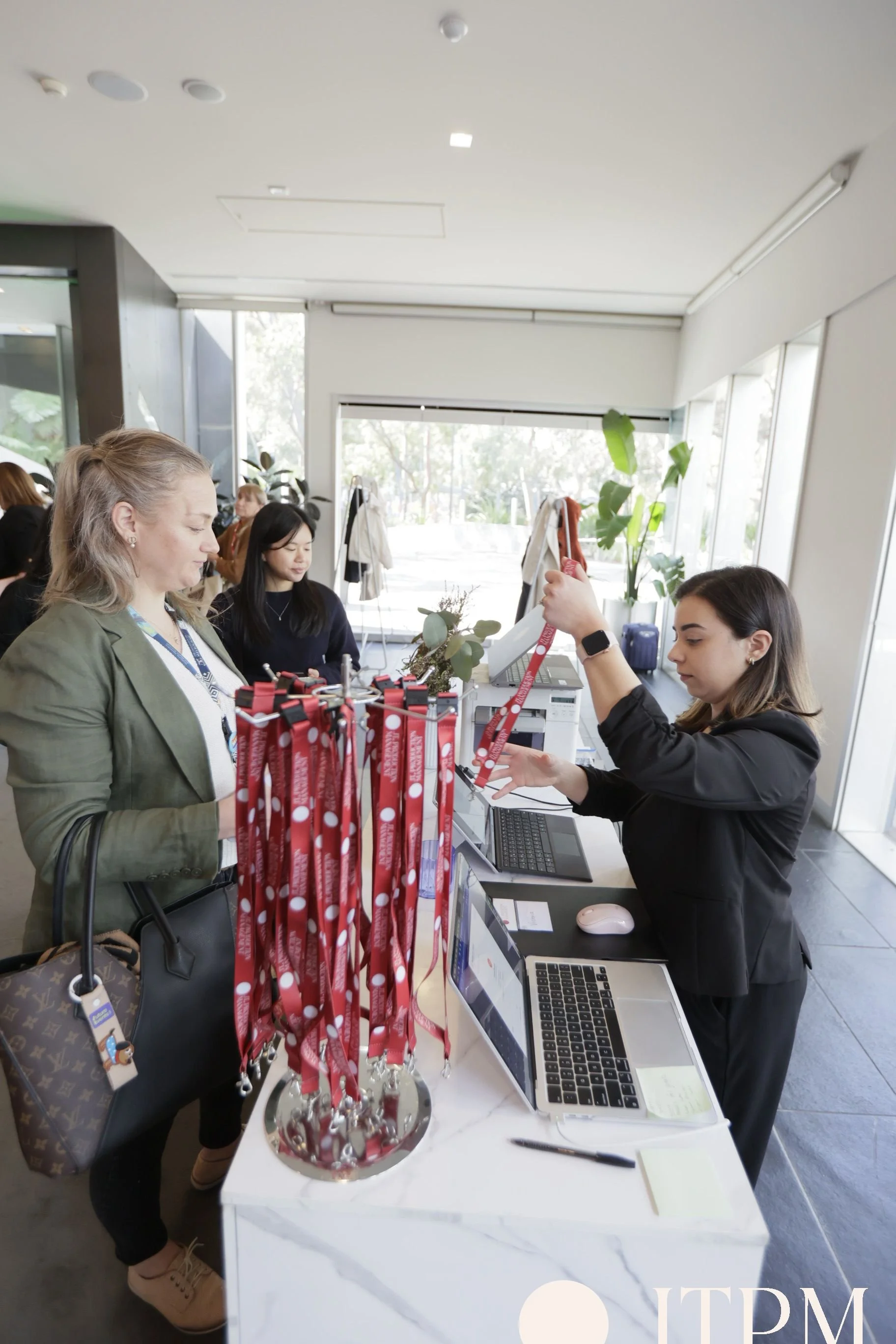 Image of guests networking during arrival and registration for a conference. An abundance of natural light pours in through the floor to ceiling windows. Guests will flow from the welcome foyer into the main event space for the presentation. 