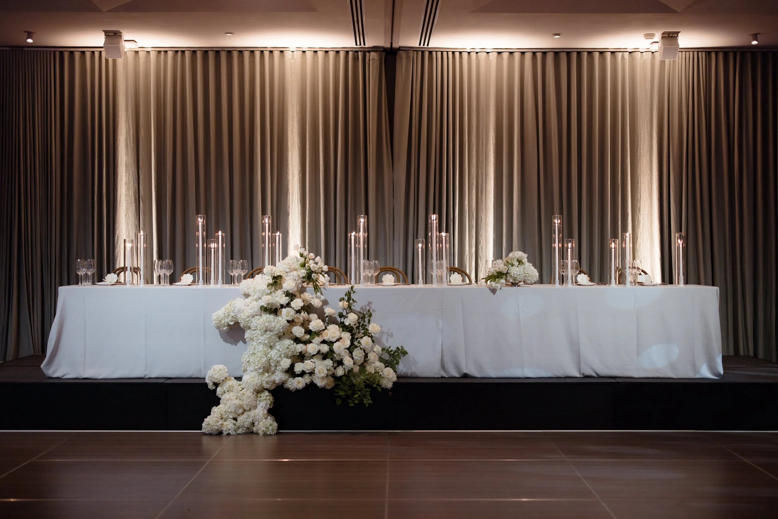 Traditional Bridal Head Table - modern romantic styling featuring pebble weave textured tablecloth, tall dinner candles in sleeves, walnut chairs, and cascading florals in neutral tones of cream, browns and greens