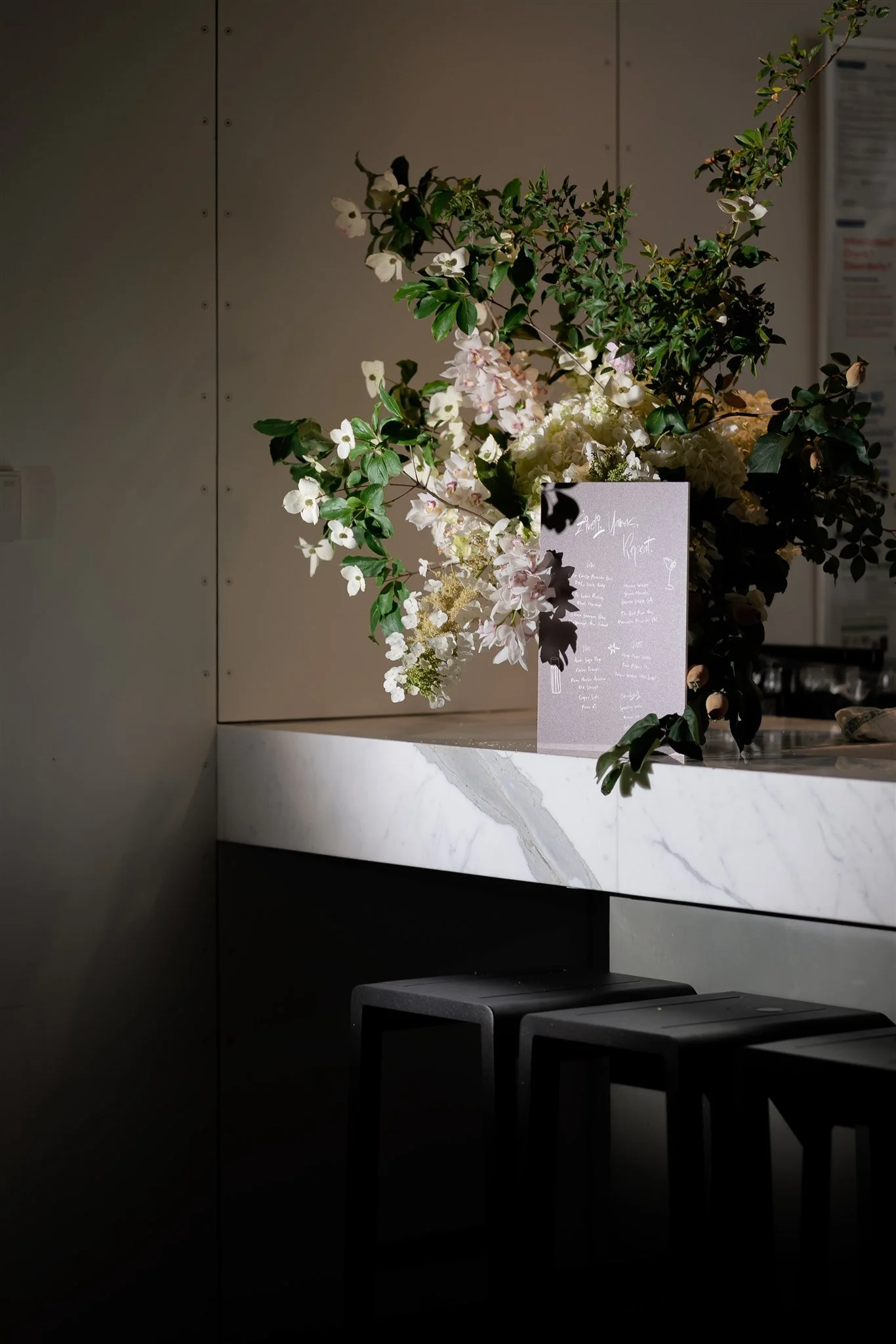 Large floral bar arrangement with luxury bar sign sitting on contemporary marble cocktail bar with stools. 