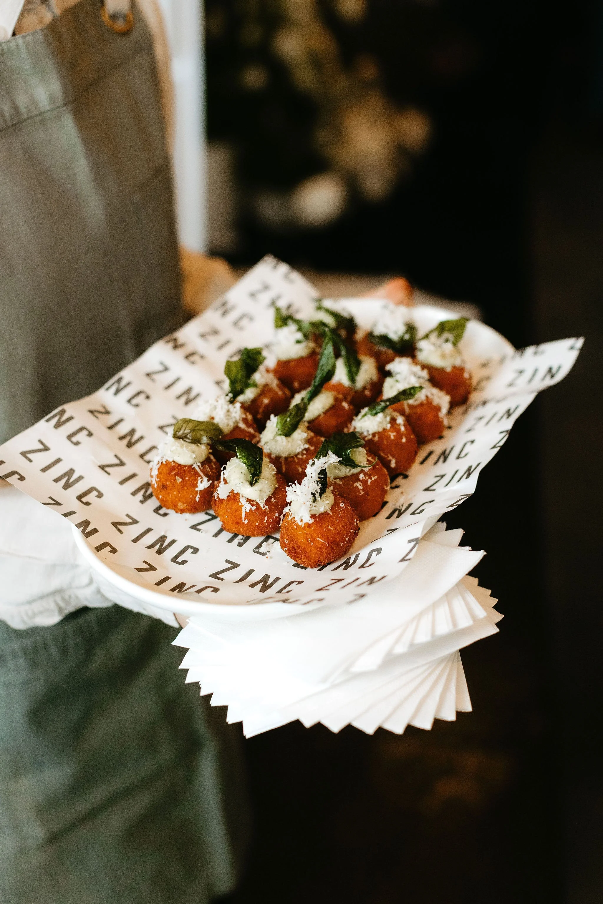 Waiter in a branded Zinc apron serves arancini as a canape to wedding guests during pre-dinner drinks