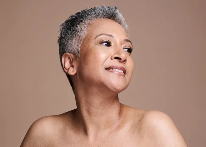 A woman with short gray hair making a confident expression, looking to the side, against a plain background.