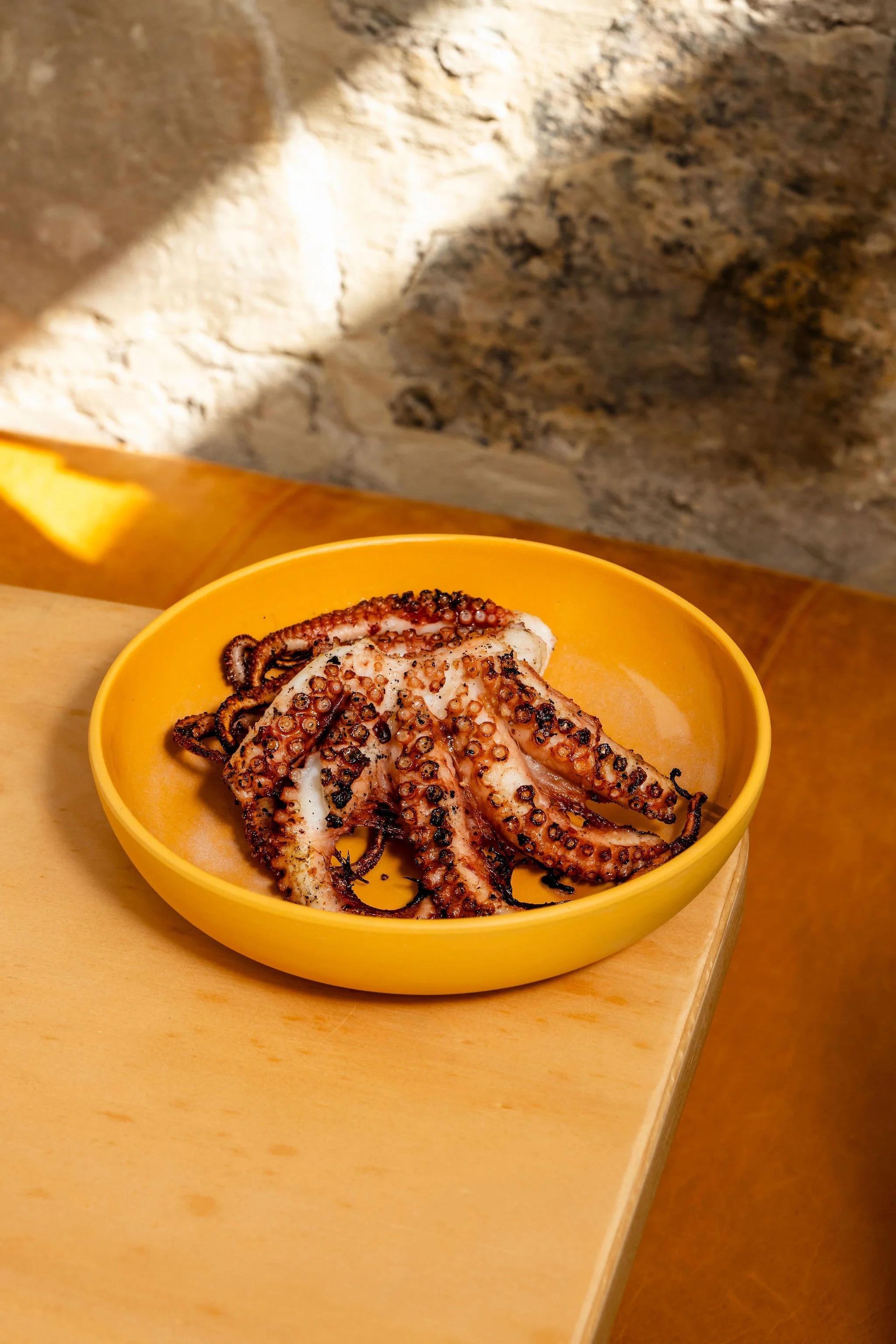 A bowl of charcoal-grilled octopus sits atop a table.