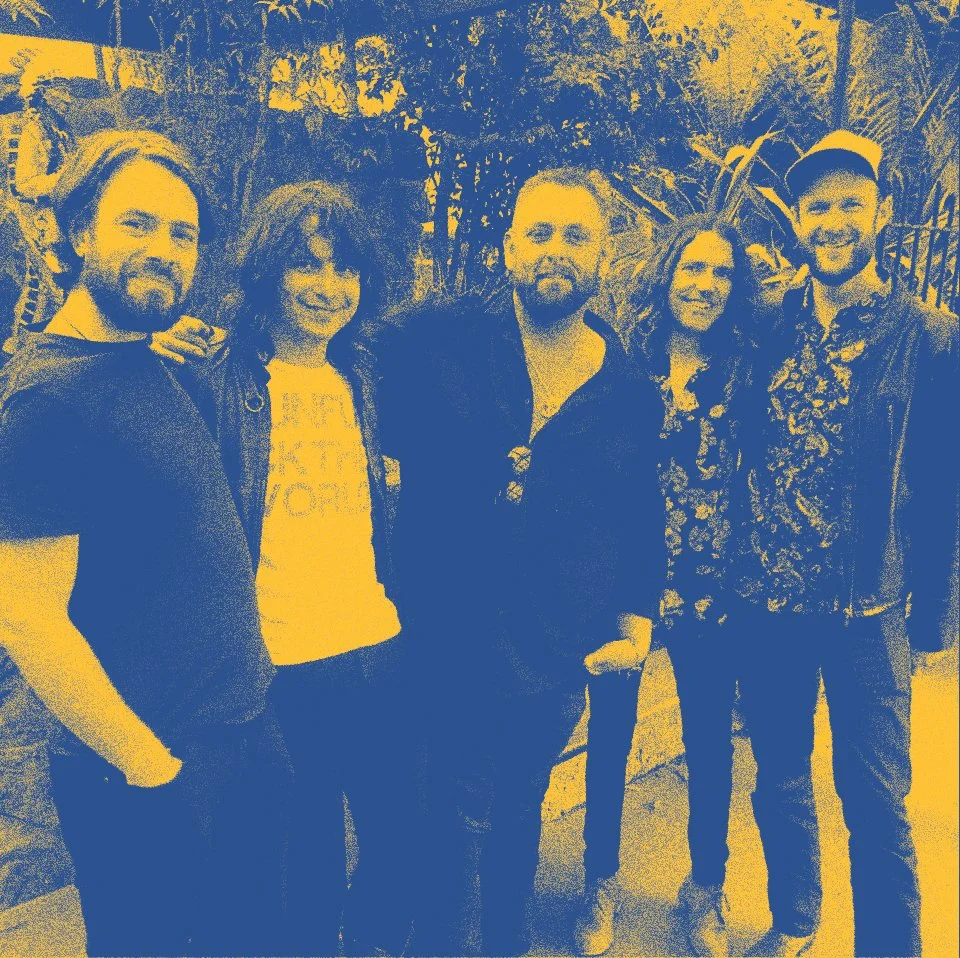 Group of five people standing outdoors, smiling, with trees and plants in the background.