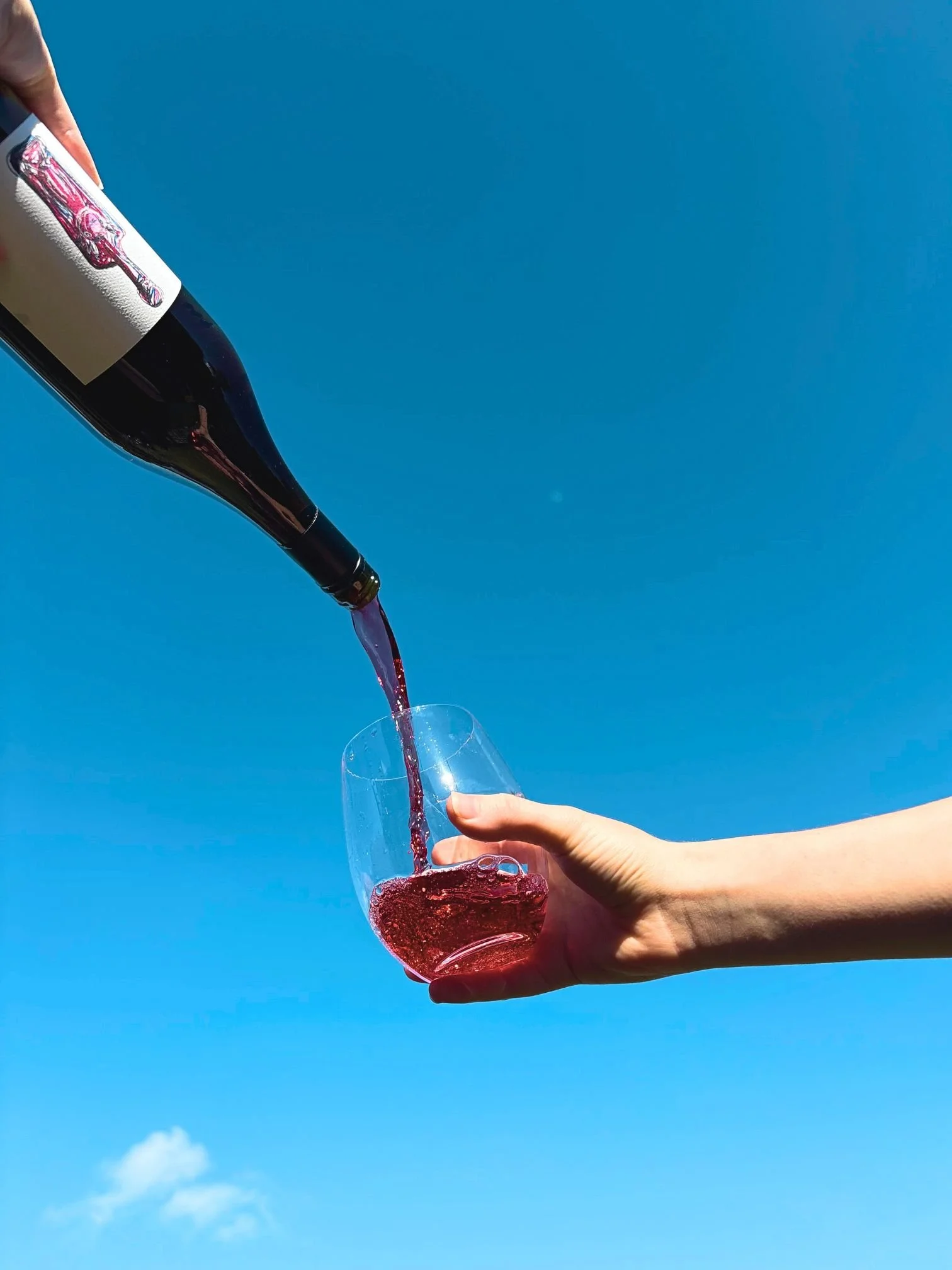 Red wine, poured into a glass in front of a blue sky