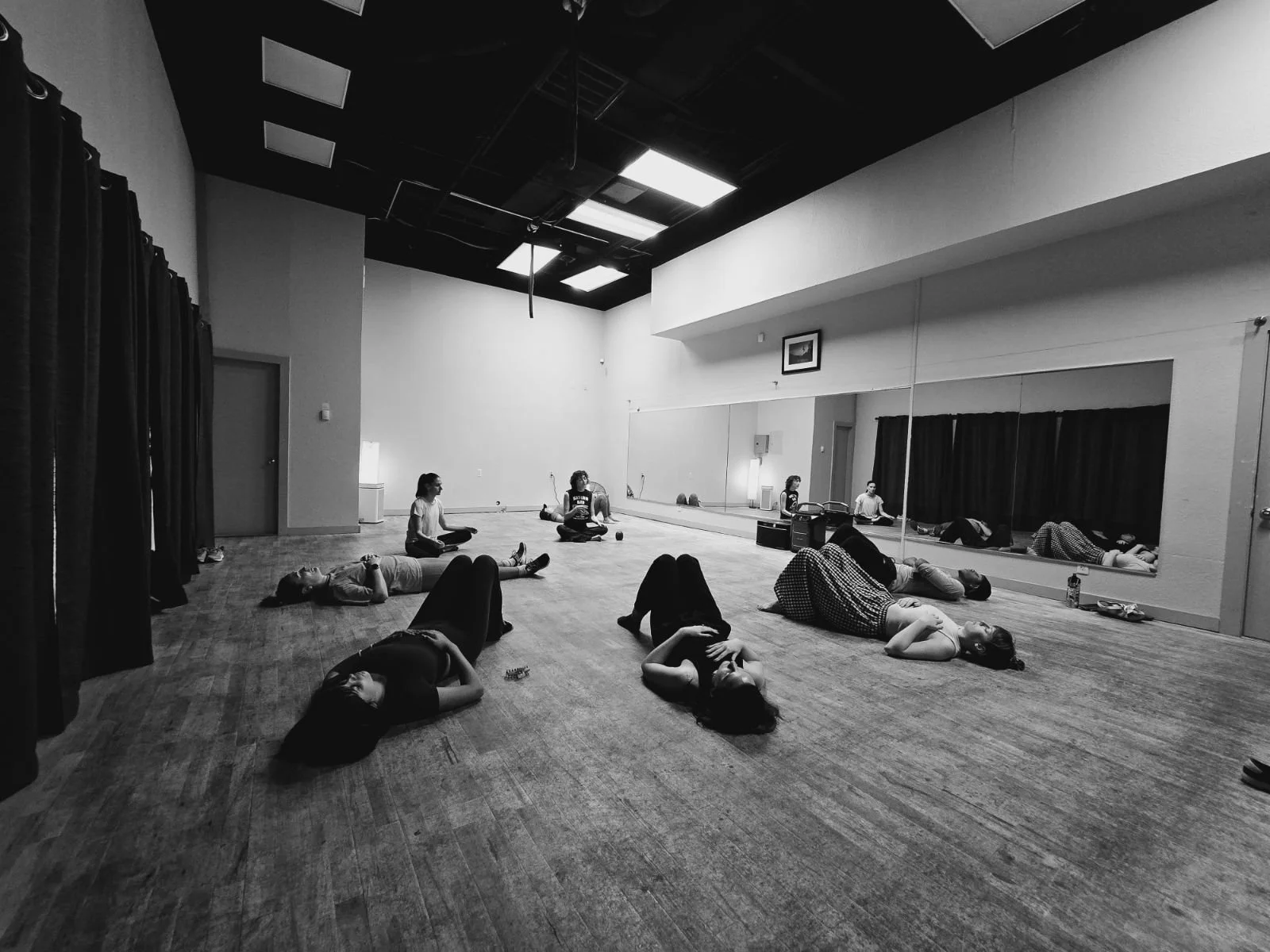 A group of people lying on the floor in a dance studio with a mirrored wall.