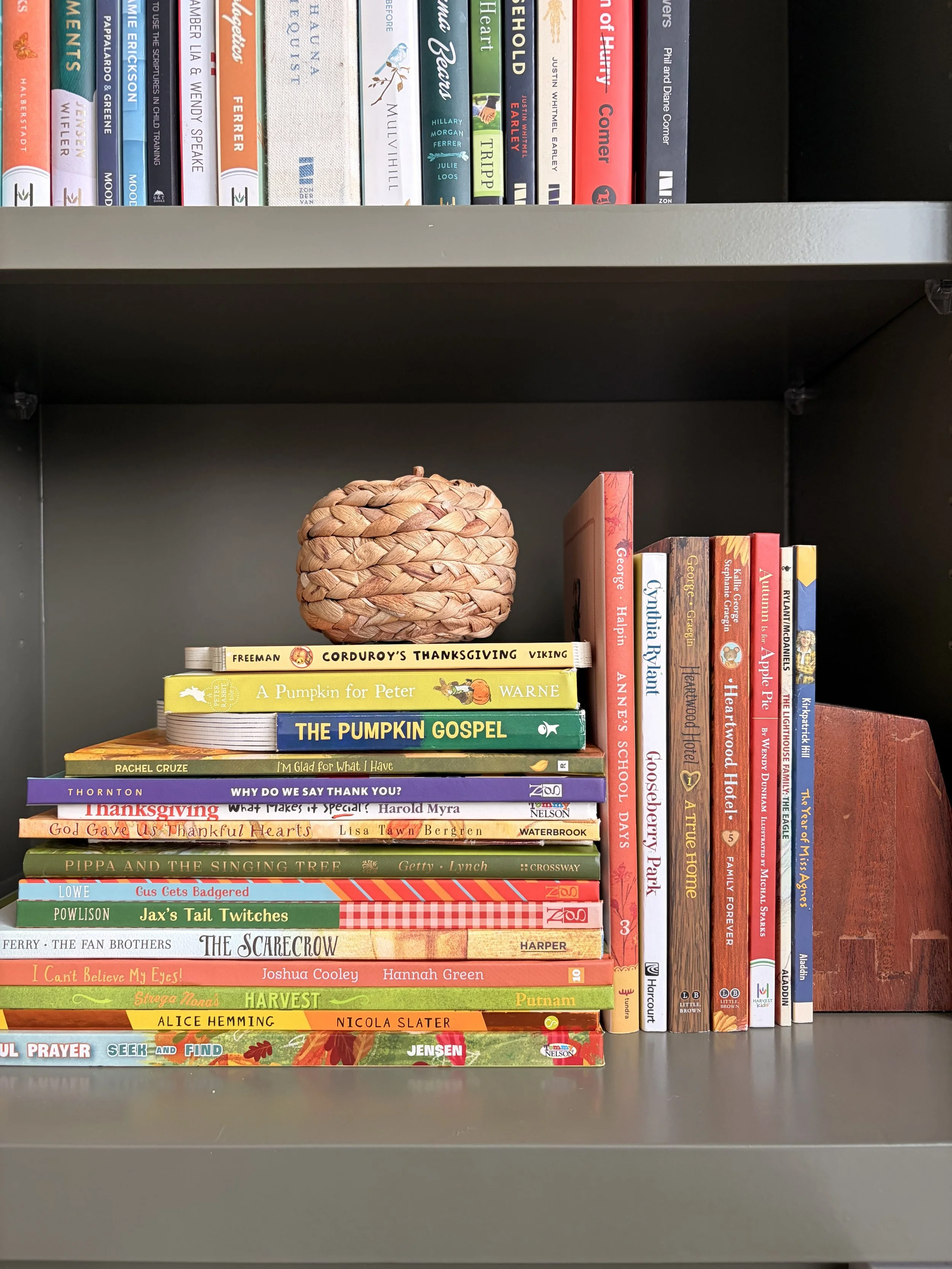 Stack of picture books, board books and chapter books about fall, halloween and thanksgiving on green home library shelves