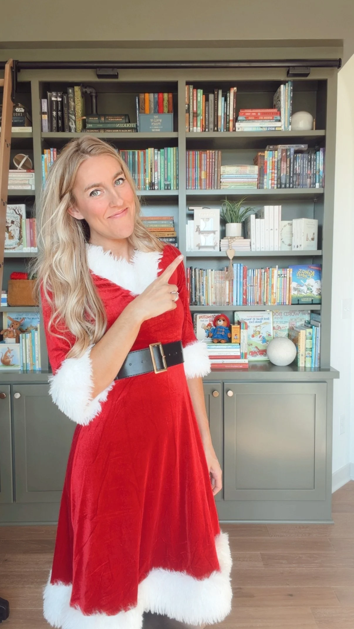 Lexi from A Good Book Hunt wearing a Christmas outfit with bookshelves in background pointing toward the signup form