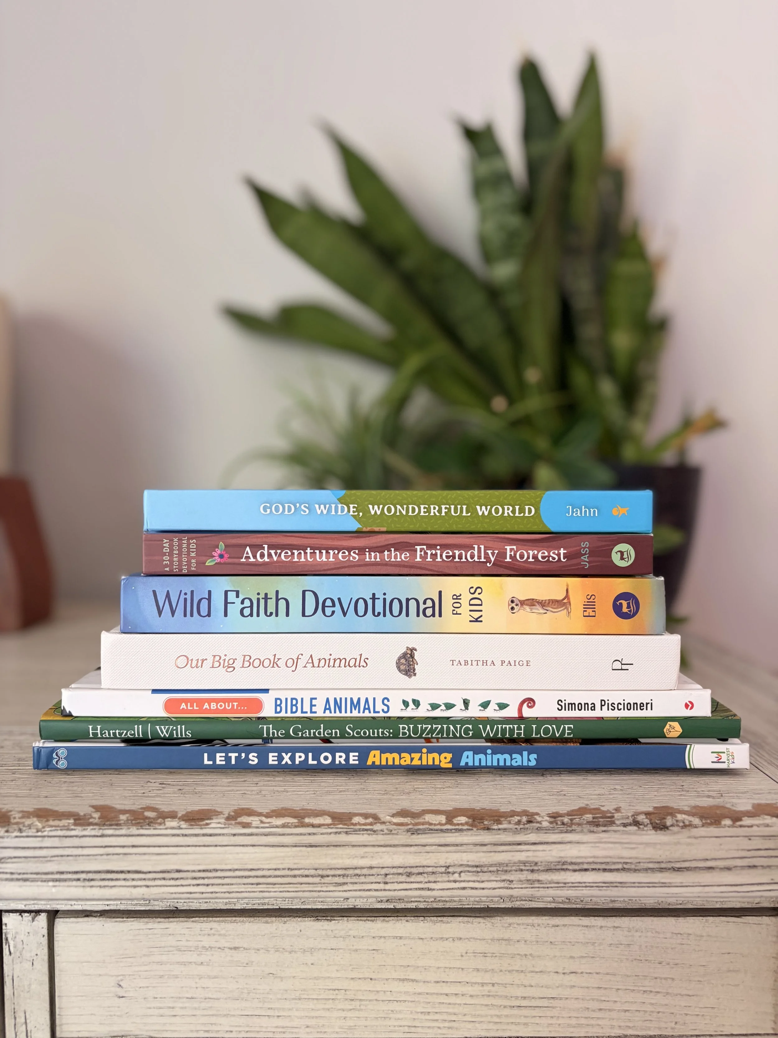 Stack of children's animal books displayed on a bookshelf with houseplants in the background, including board books, picture books, devotionals, and chapter books for animal-loving kids