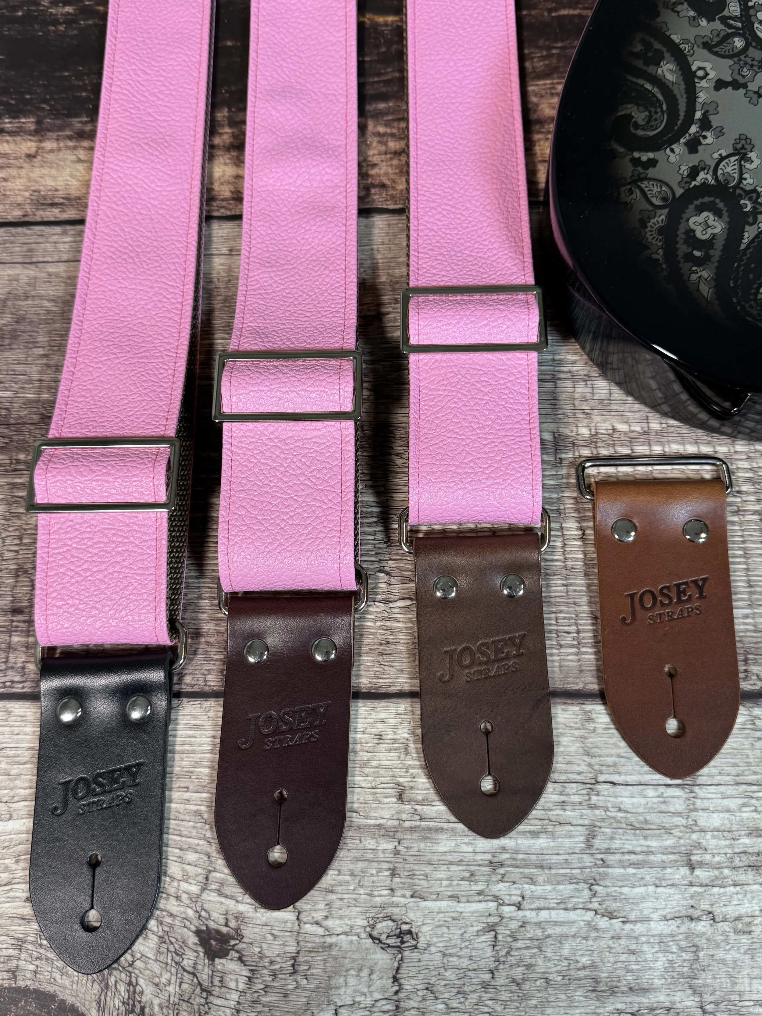 Bubblegum pink tolex guitar straps on wooden floor with guitar.