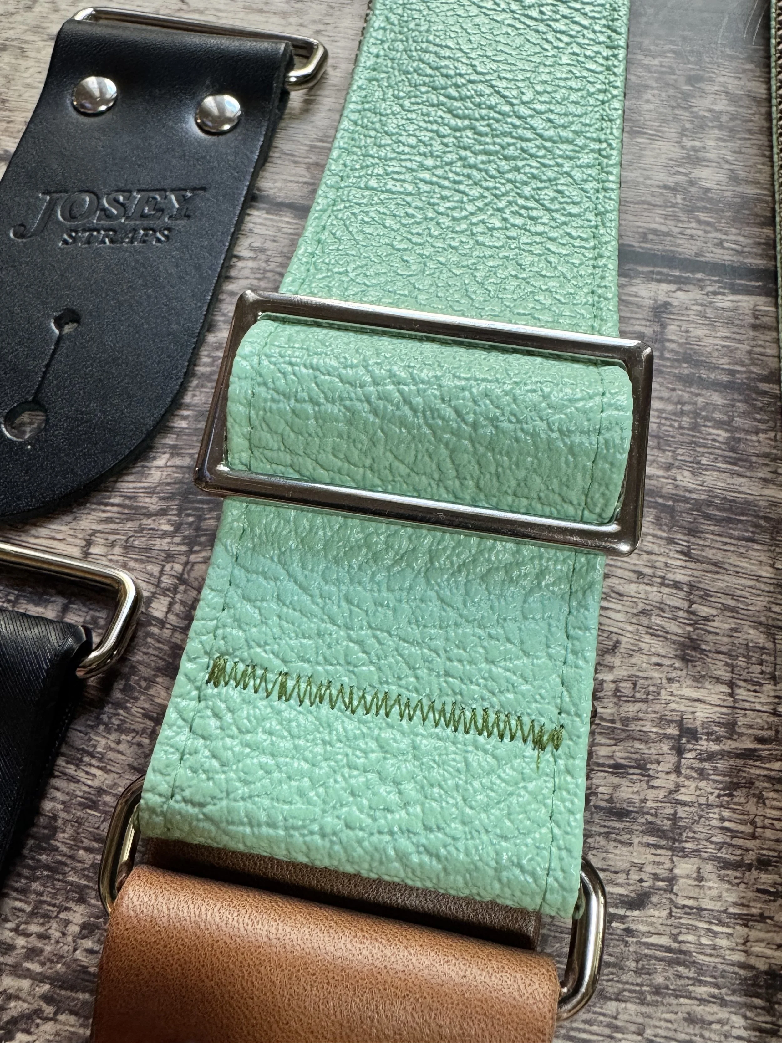 Seafoam green guitar straps on wooden floor.