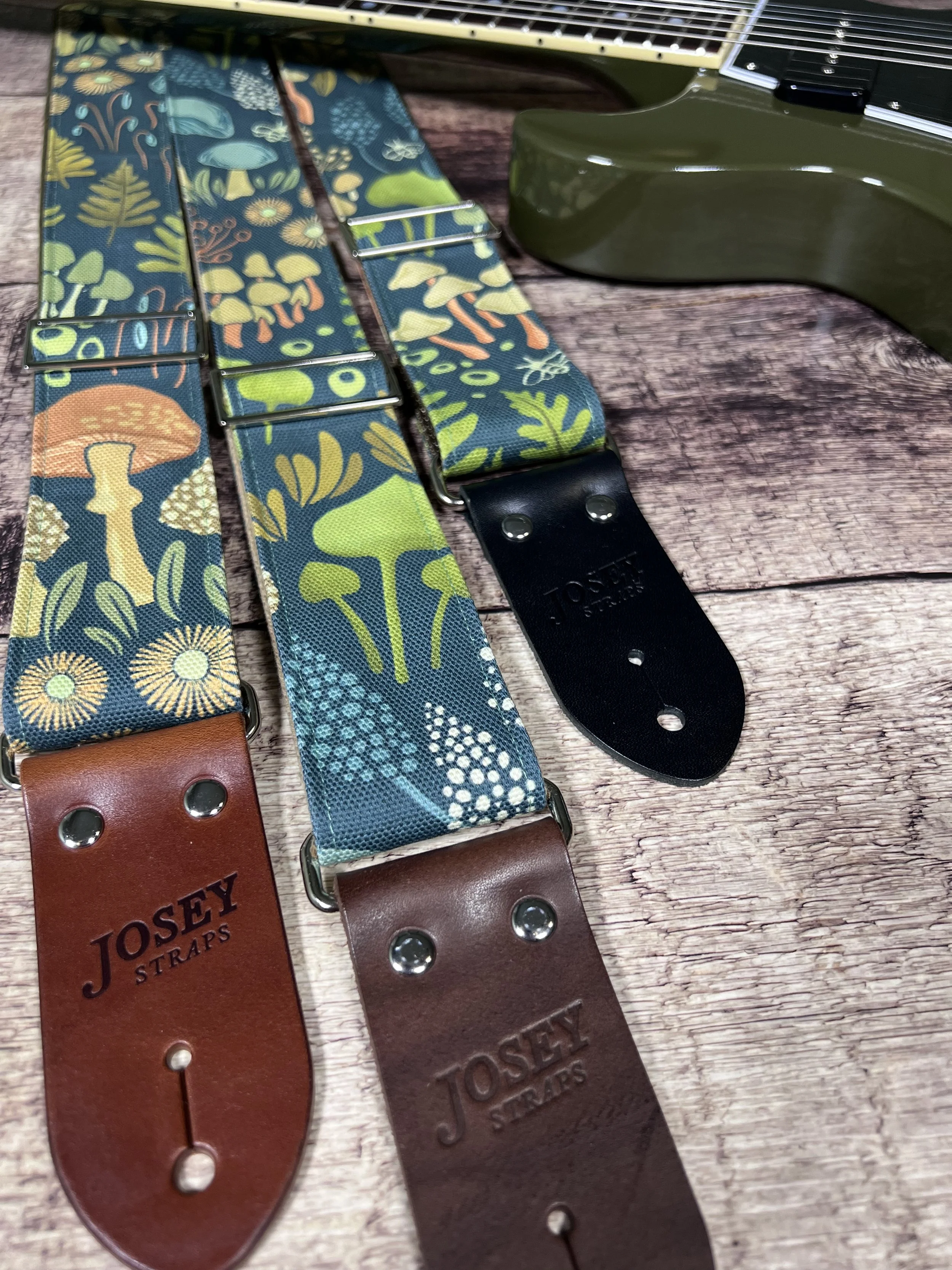 Dark botanical guitar straps on wooden backdrop.
