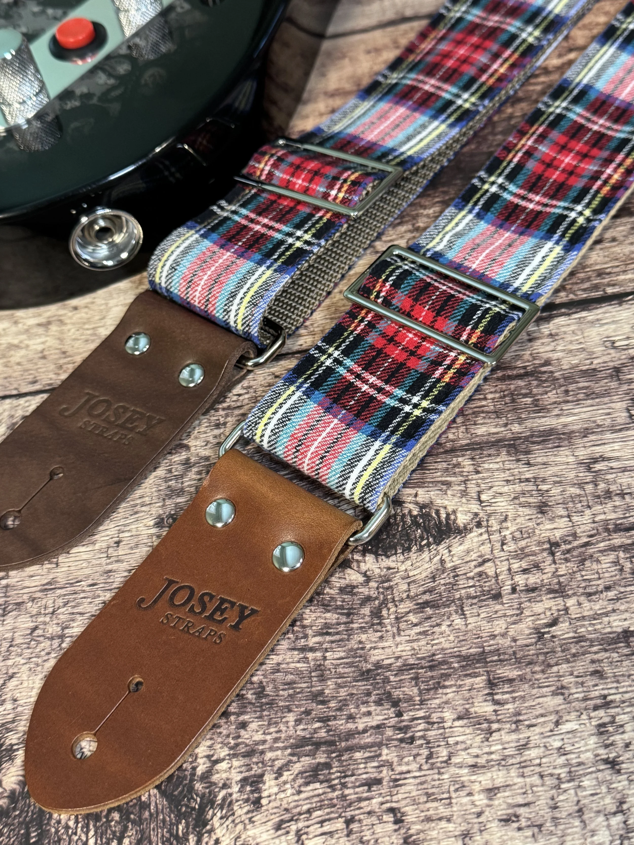 two red and blue plaid with premium leather ends laying next to a black guitar on wood background