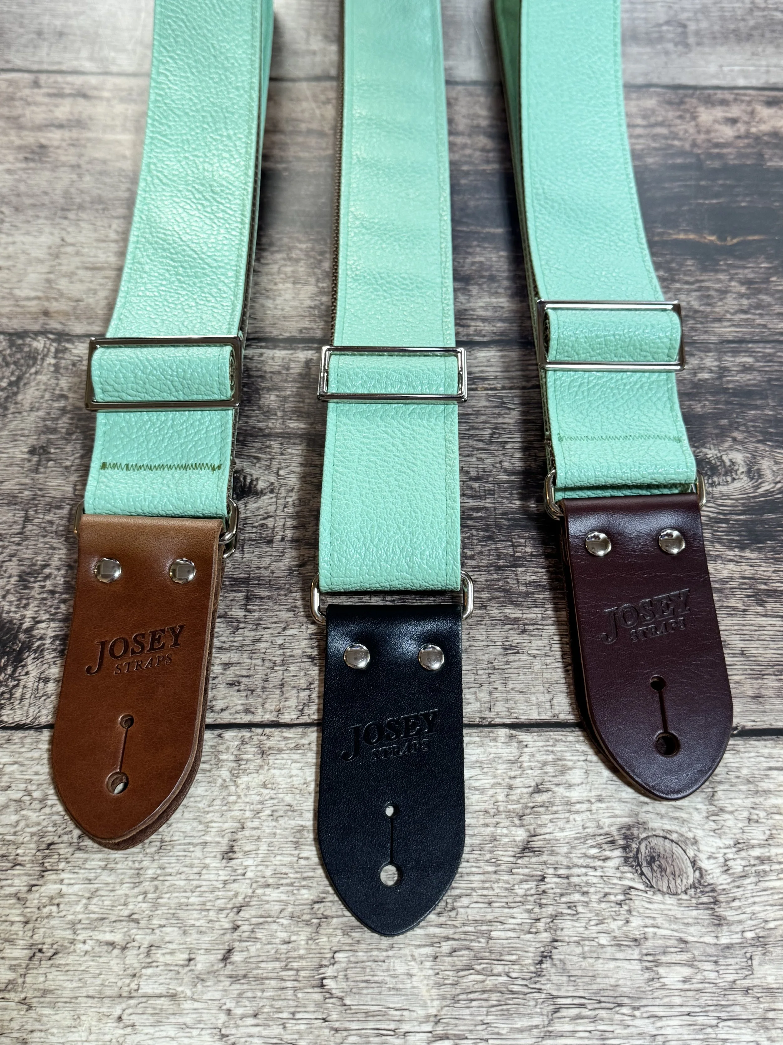 Seafoam green guitar straps on wooden floor.
